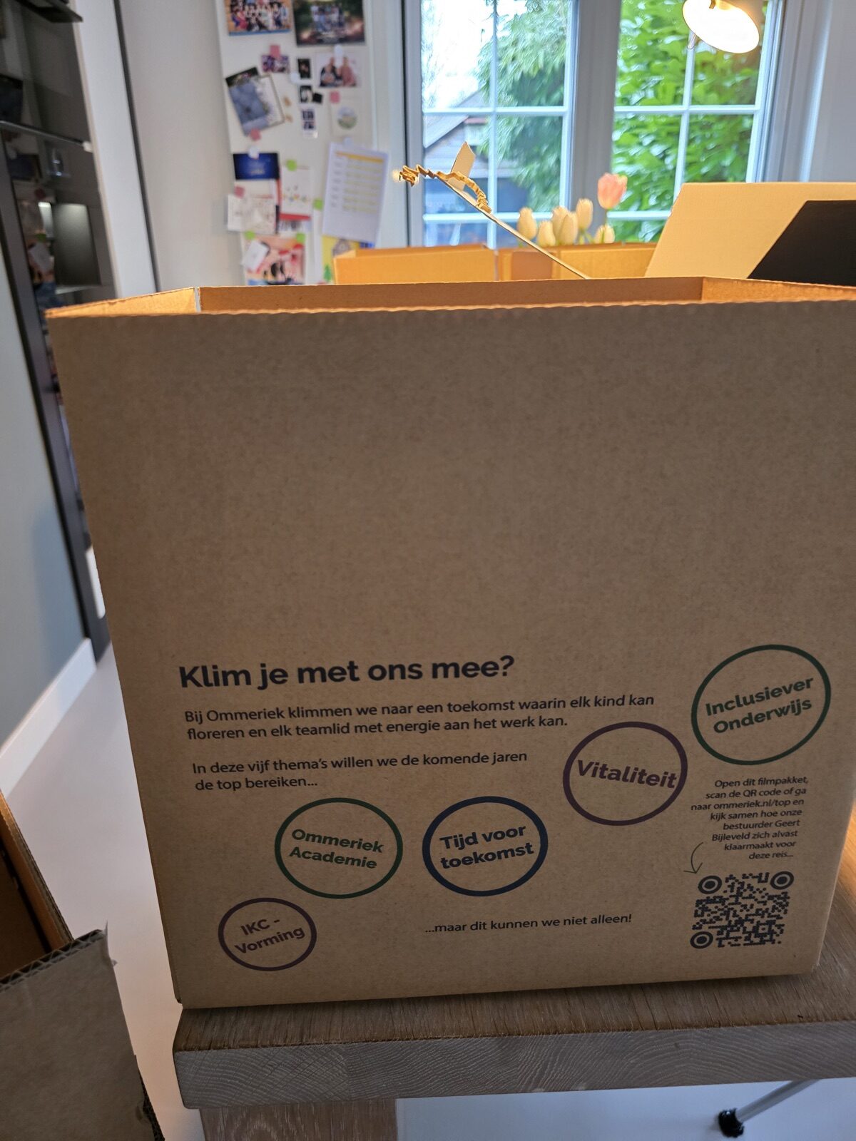 Kartonnen vouwdoos met opdruk Klim je met ons mee, de vijf thema's in gekleurde cirkels en een QR-code naar de landingspagina